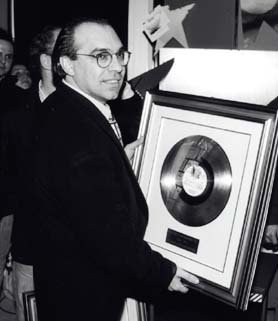 Man in a suit and glasses holding a framed platinum record award at an event.