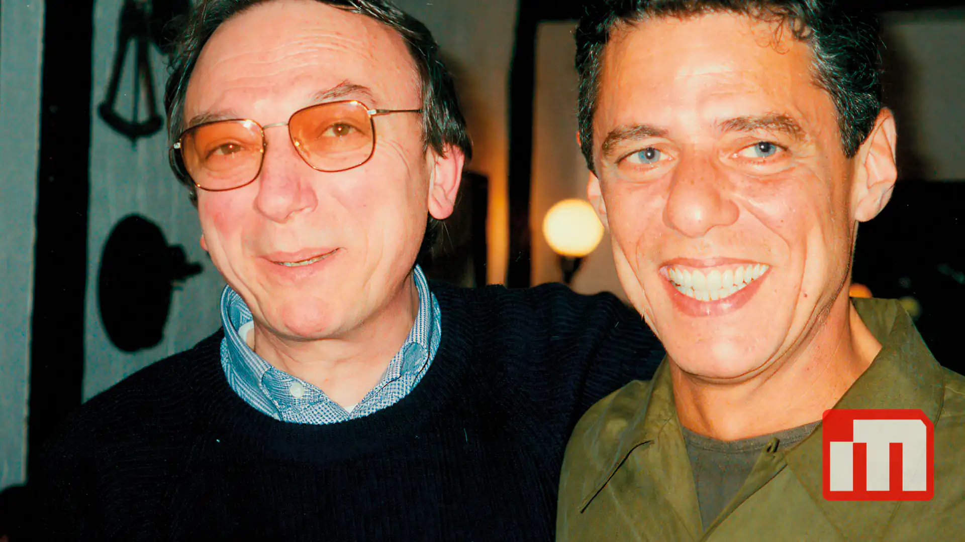Two men posing and smiling for a close-up photo, one wearing glasses on the left and the other in a green shirt on the right.