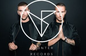 Two men in black jackets pose side by side with a large white Counter Records logo overlaying the image.