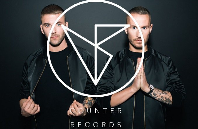 Two men in black jackets pose side by side with a large white Counter Records logo overlaying the image.